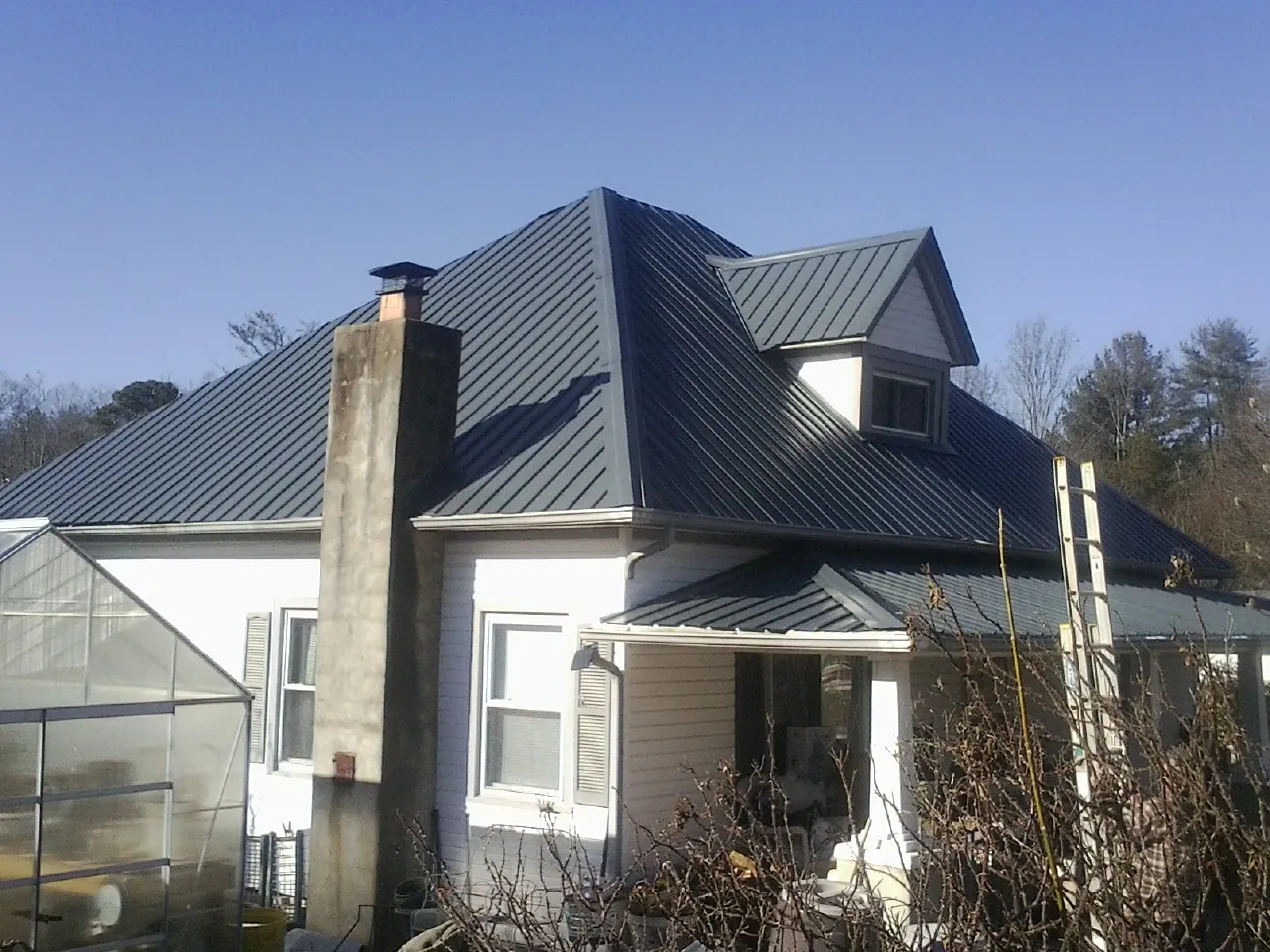 Dark blue standing seam metal roof on a white farmhouse with dormer — Slate & Tile Roof Repair by Roofing Brothers in Buchanan