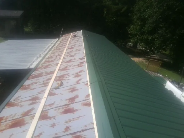 Old rusted panels beside newly installed green metal roofing — Wind Damage Roof Repair by Roofing Brothers in Buchanan